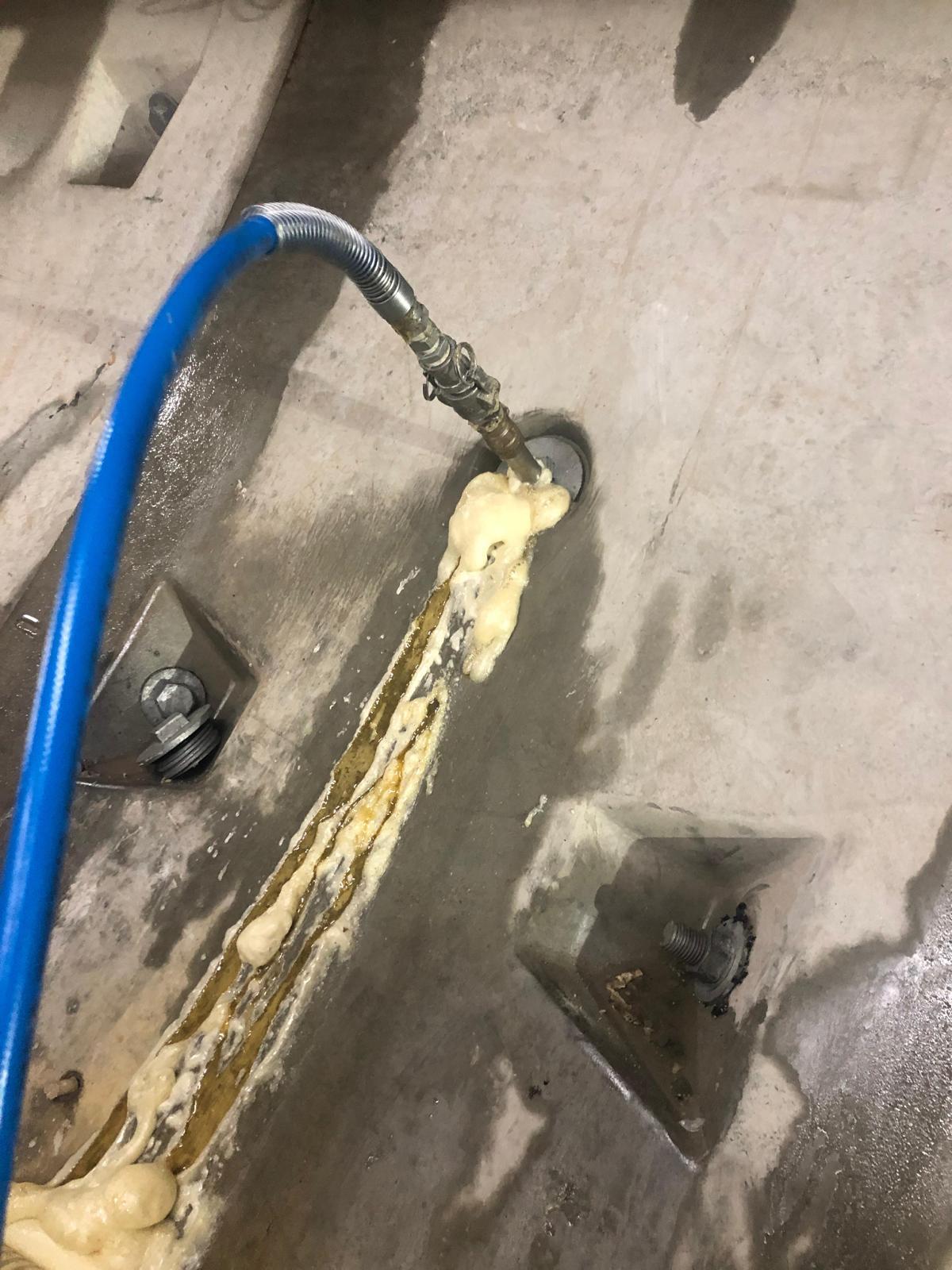 A detailed shot of an industrial blue hose connected to a nozzle, injecting expanding foam grout into a seam between concrete structural segments